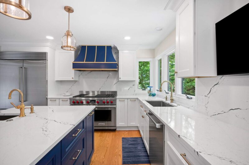 Kitchen with brass faucets at the island and sink, white quartz counters and a blue range hood