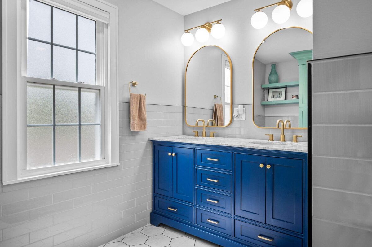 Bathroom with a blue double vanity, brass faucets and arched brass-framed mirrors