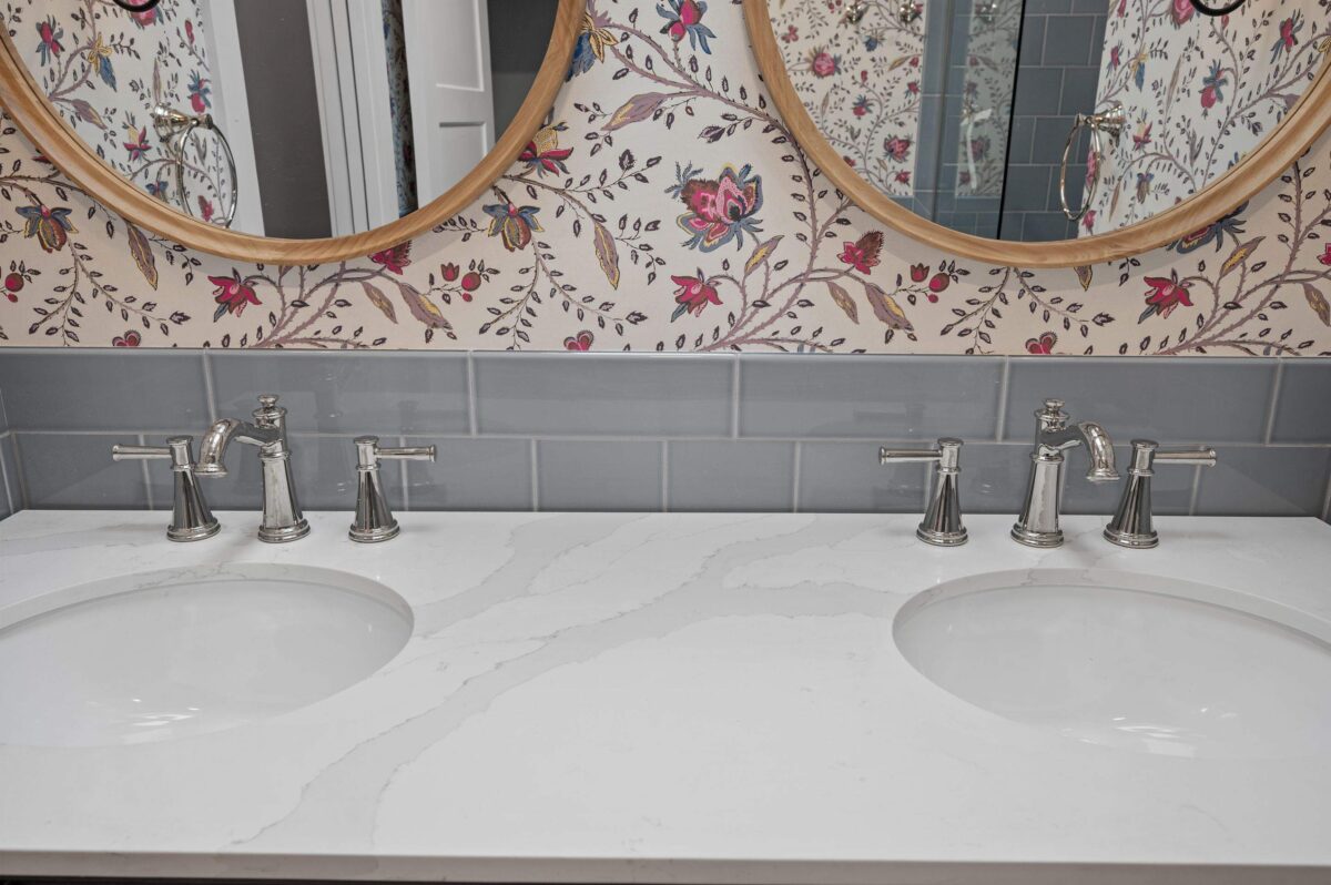 Double vanity with two oval undermount sinks in a white veined quartz top with polished nickel faucets and round wood-framed mirrors