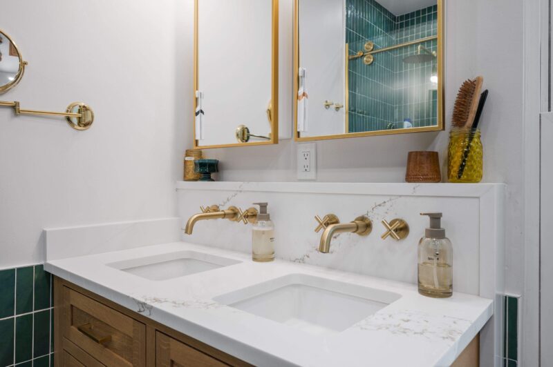 Wall-mounted brass faucets with cross handles over two undermount sinks on a white quartz top