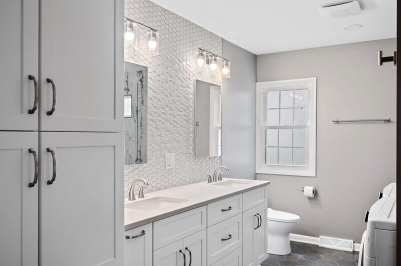Brushed nickel widespread faucets on a white double vanity with a hexagon tile wall