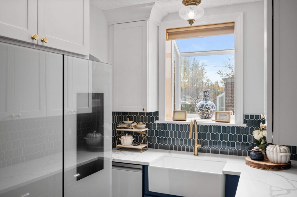 White kitchen with a farmhouse sink under a window and blue hexagon tile backsplash