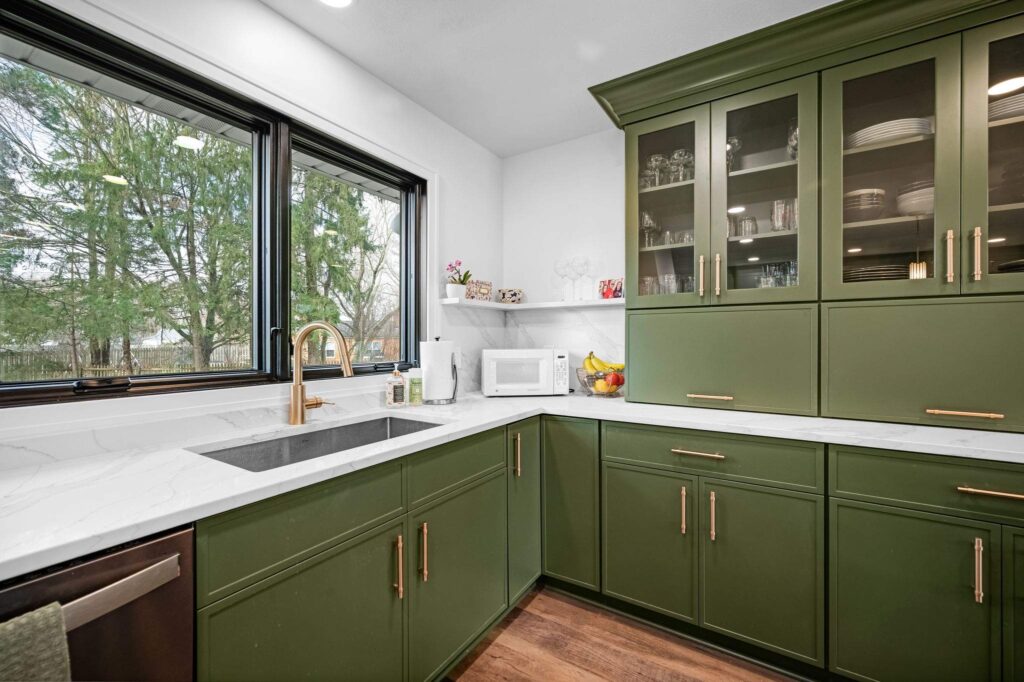 Green kitchen with a stainless steel sink under a window